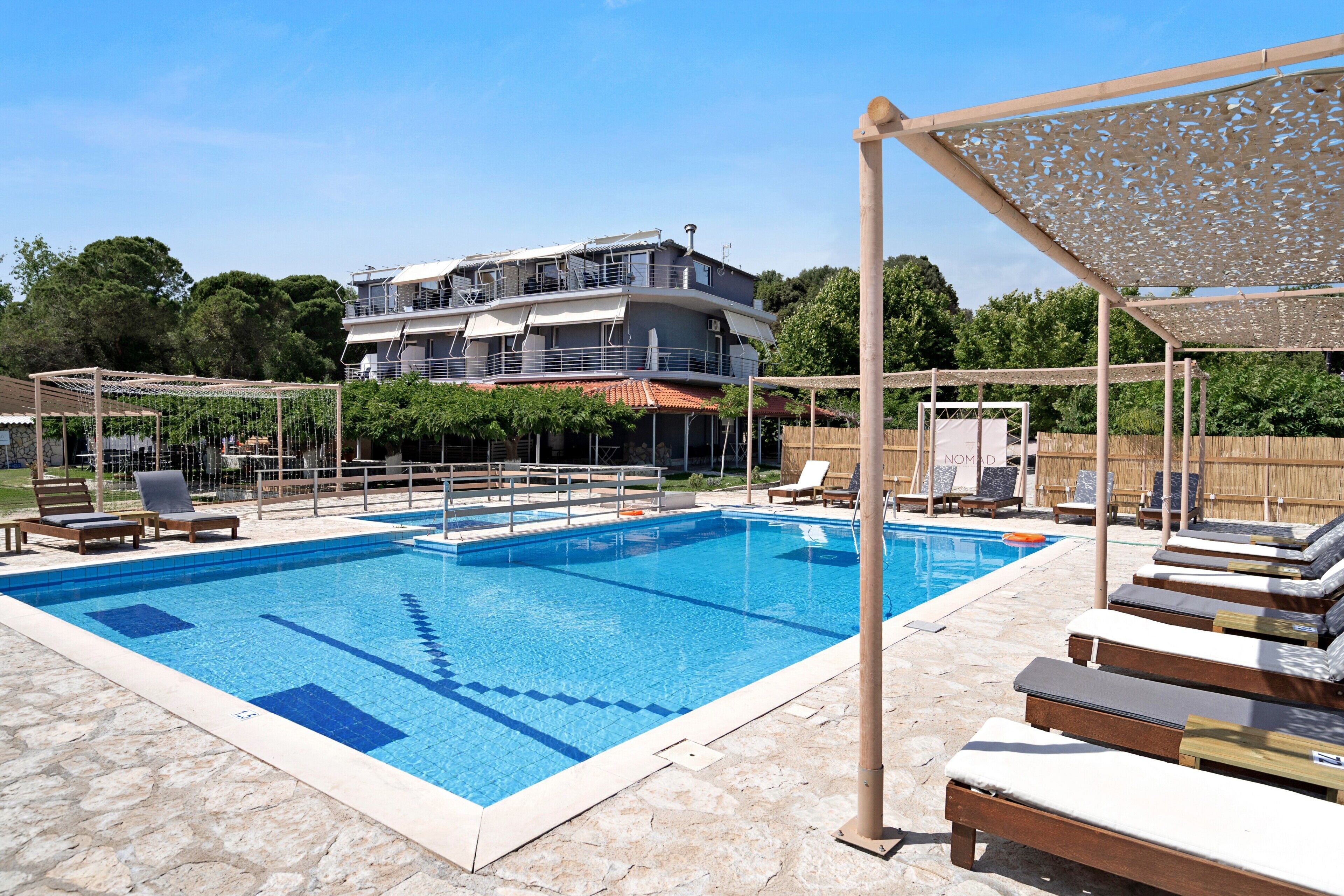 Ein Pool mit Liegestühlen, einer Pergola und einem mehrstöckigen Gebäude im Hintergrund.