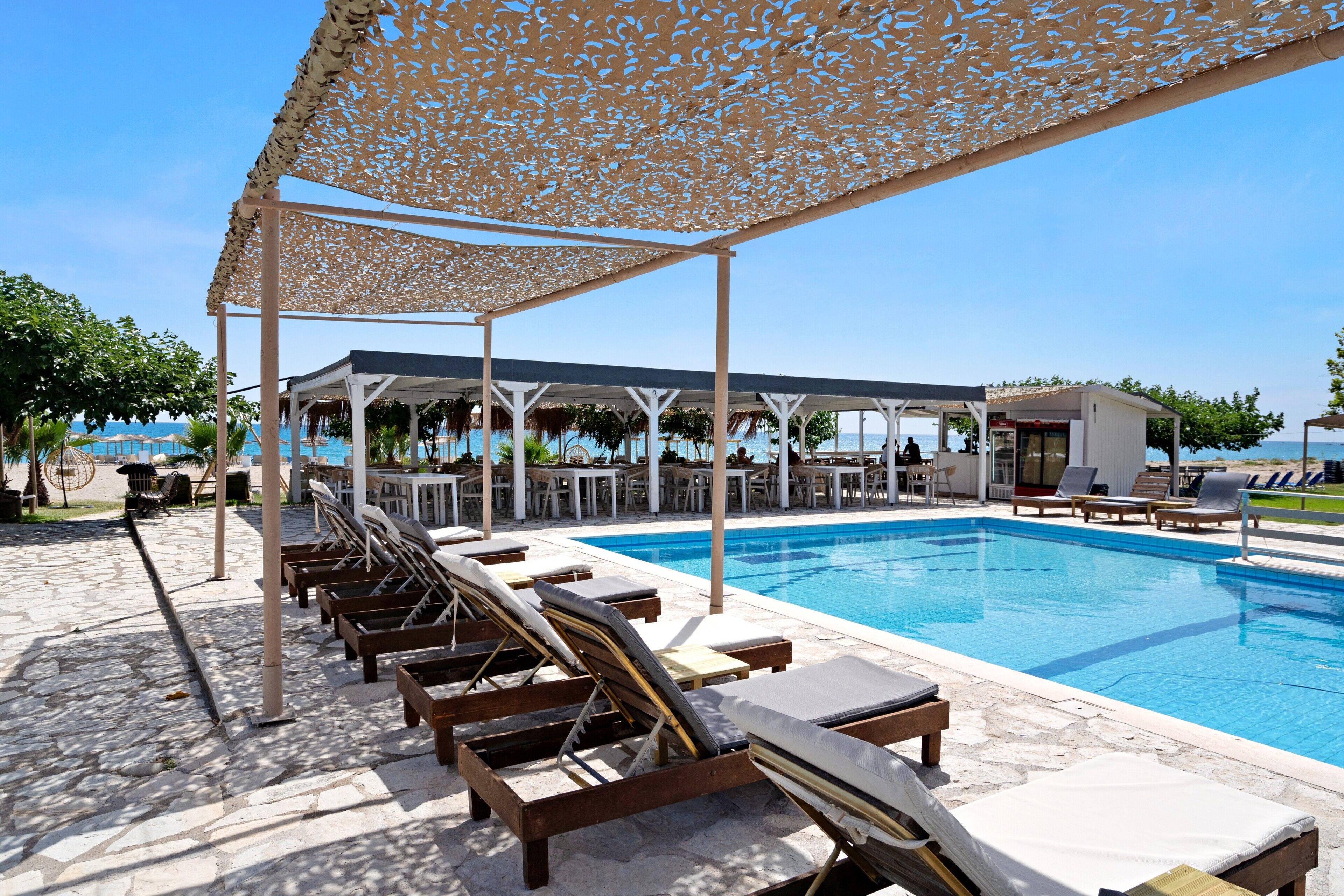 A poolside area with lounge chairs, a covered seating area, and a view of the sea.