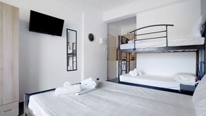 A hotel room with a bunk bed, a flat bed, a TV mounted on the wall, and a wardrobe. - Studio Apartment 'Iguana 9' with Sea View, Wi-Fi and Air Conditioning (Preveza)
