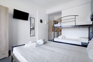 A hotel room with a bunk bed, a flat bed, a TV mounted on the wall, and a wardrobe.