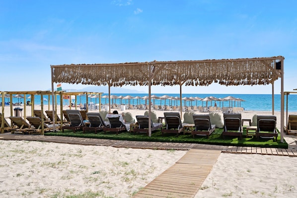 A beachside lounge area with wooden loungers and a thatched canopy, overlooking the sea.