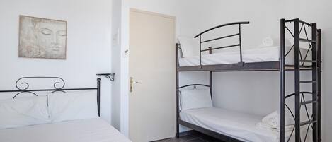 Huoneessa on yksi sänky, kerrossänky ja ovi.