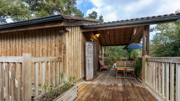 A wooden cabin with a covered porch, a map sign, and outdoor seating. - Exceptional Treehouse Chalet in Labenne Océan – Nature, Comfort & Privacy 400m from Beach (Labenne)