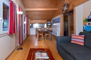 A cozy interior with a dining area, wooden ceiling, and a sofa with a colorful pillow.