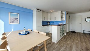 Una cocina moderna con armarios blancos, pared azul y una zona de comedor con mesa y sillas de madera.