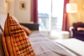 Una cama con un cojín de cuadros, una ventana con vistas y una lámpara sobre una mesita de noche.