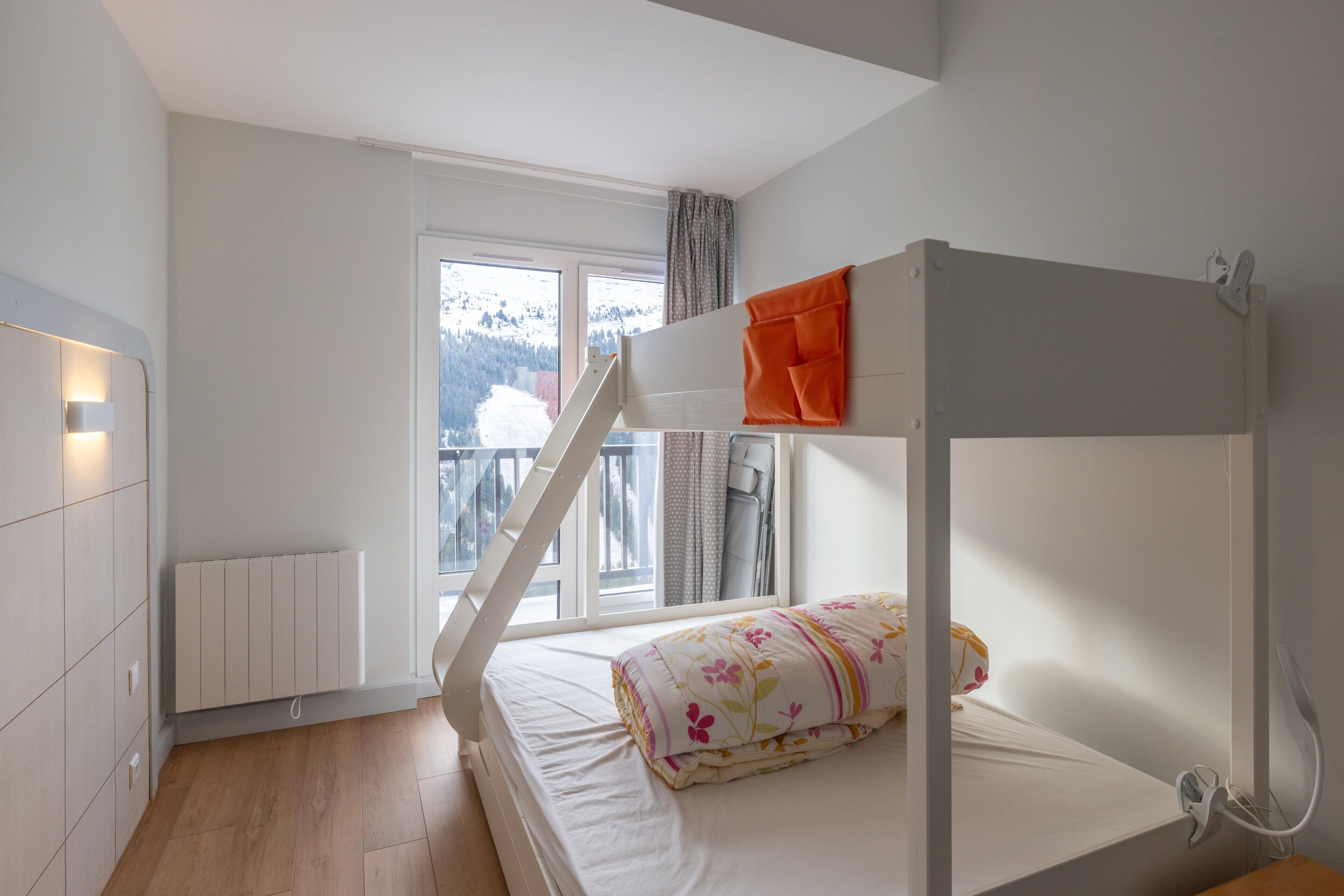 Ein Stockbett mit Blick auf einen verschneiten Berg, ein Heizkörper und ein Fenster mit Vorhängen.