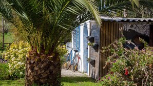 Un jardin avec un bac à fleurs en pierre, un vélo et une petite construction en bois.