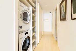 A laundry room with stacked washing machines, a hallway with a door at the end, and a framed picture on the wall. - "Sitges Suites" Apartment with Sea View, Private Terrace and Wi-Fi (Sitges)