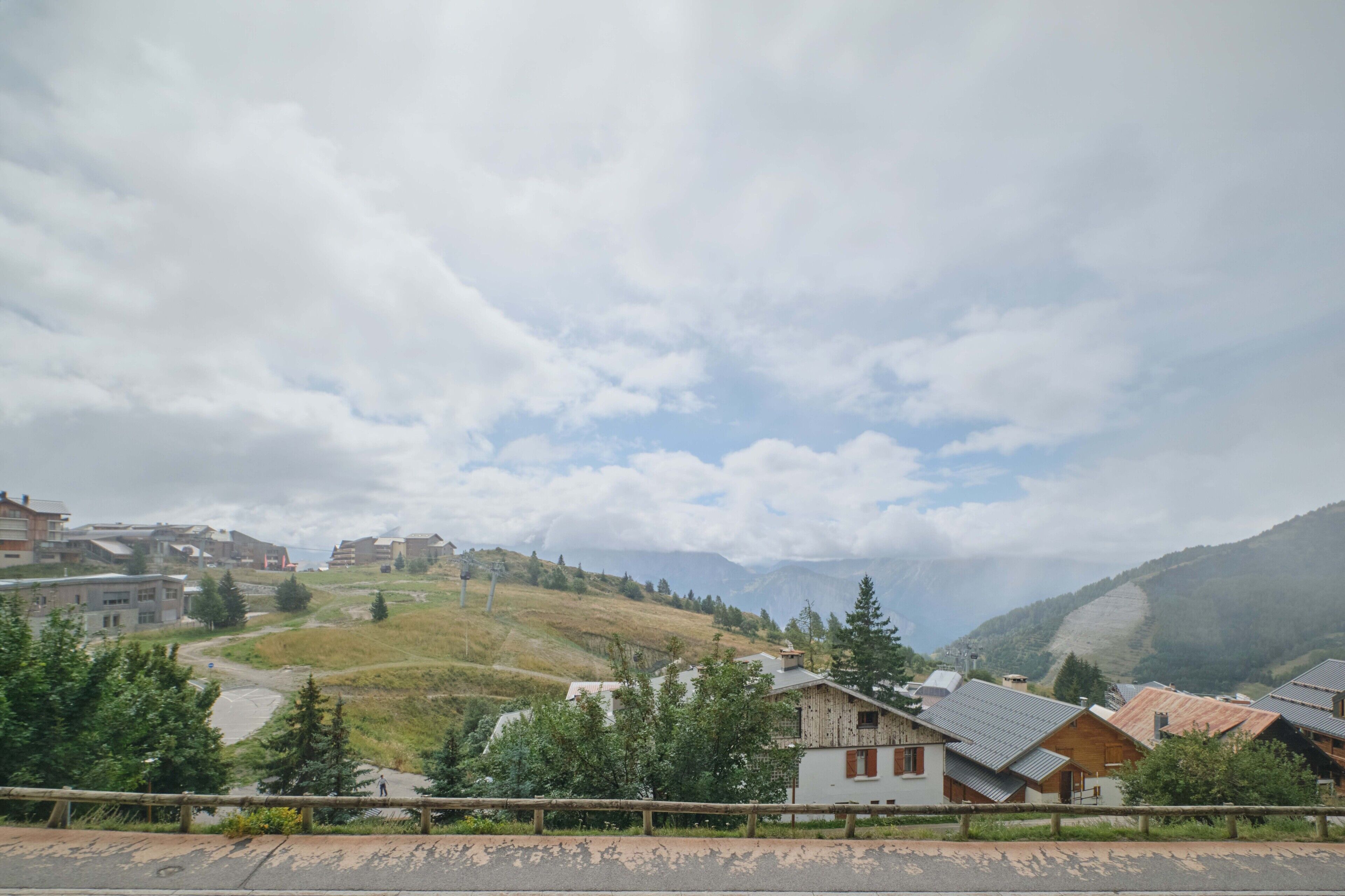 A mountainous village with houses, a road, and a guardrail.