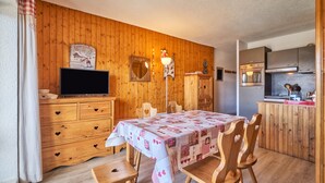 Un interior de madera con una mesa de comedor, sillas, un televisor, un espejo y una zona de cocina.
