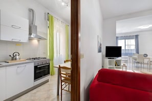 A modern kitchen with white cabinets, a gas stove, and a built-in oven. There is a dining area with a table and chairs, and a red sofa in the foreground. - Apartment 'Casa Rosa' with Private Terrace and Wi-Fi (Loano)