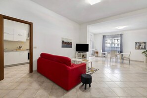 Uma sala de estar moderna com um sofá vermelho, um banquinho preto pequeno, uma TV e uma área de jantar com mesa e cadeiras.