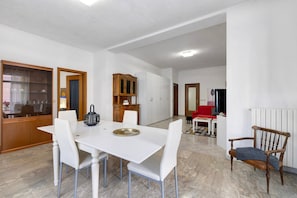 Uma área de refeições com mesa e cadeiras brancas, um armário de madeira e um radiador.