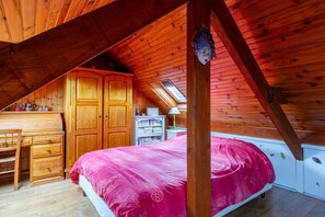 Et soveværelse på loftet med trægulv, seng, skrivebord og garderobe.