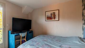 Een slaapkamer met een bed, een bureau met een televisie, een stoel en een schilderij aan de muur.