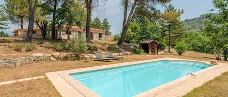 A swimming pool with lounge chairs, surrounded by trees and a stone wall.
