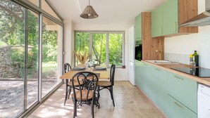 A modern kitchen with large windows, a dining area with a table and chairs, and green cabinetry. - House with Pool at the Foot of the Vineyards in the Luberon – Tilleul T3 Maison Marvic (Apt)