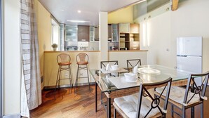Une cuisine moderne avec un coin repas, comprenant une table en verre et des chaises en osier.