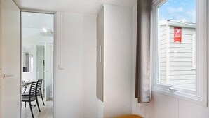 A room with a bed, a window, a door, and a view of a building outside.