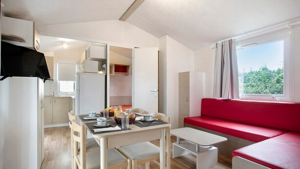 Una cocina compacta con armarios blancos, una mesa de comedor con sillas y un sofá rojo junto a una ventana.