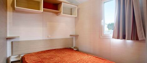Un dormitorio con cama, estantes empotrados, una ventana con cortinas y una mesita de noche.