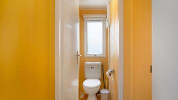 Un pasillo estrecho que conduce a un baño con inodoro, un cesto de basura y una ventana.