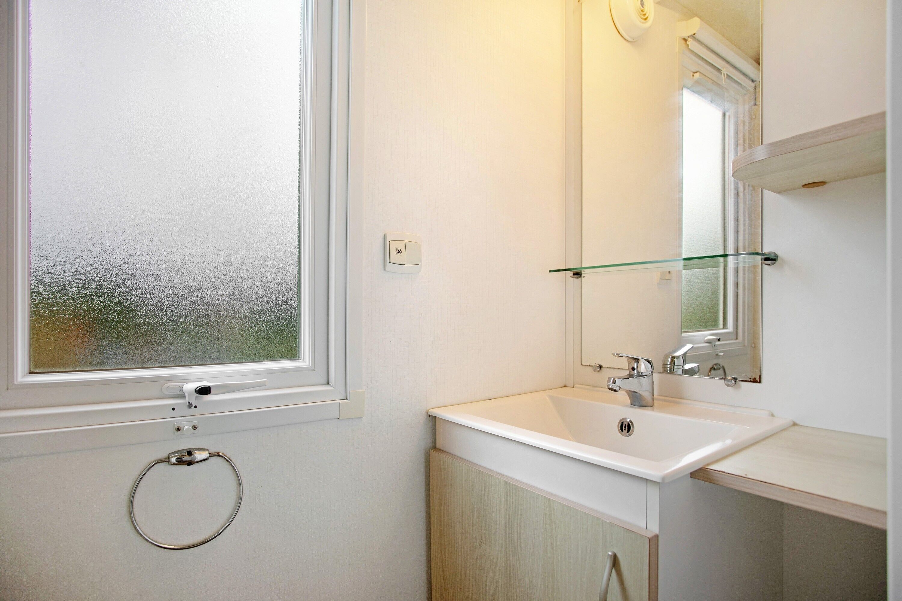 Une salle de bain avec une fenêtre, un lavabo, un miroir et un porte-serviette.