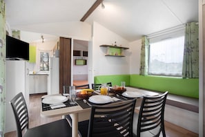 Uma sala de jantar com uma mesa posta para quatro pessoas, uma cozinha ao fundo e uma janela com vista.