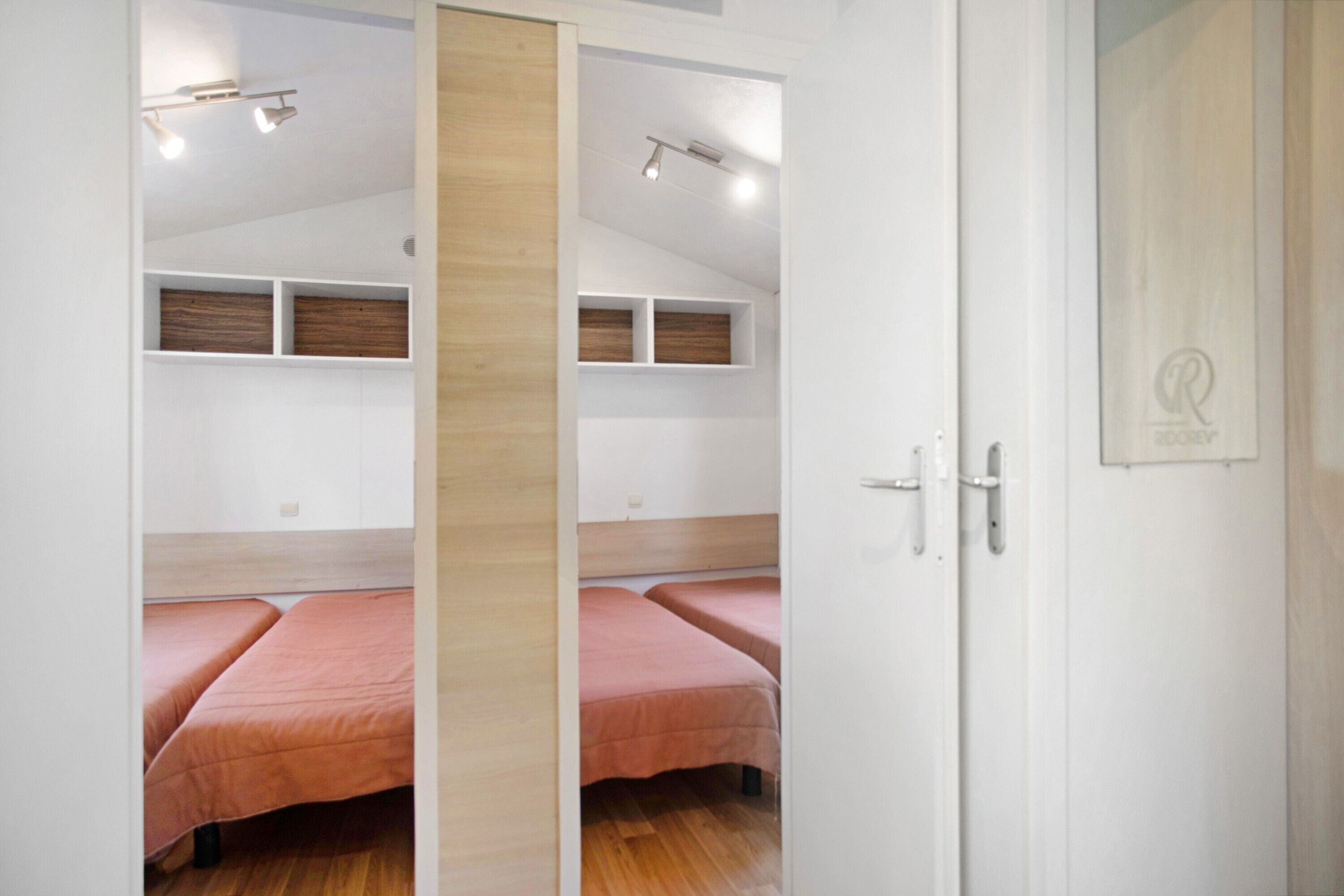 Une chambre avec deux lits, des étagères en bois et une porte ornée d’un logo.