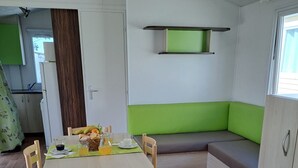A compact living space with a dining table, chairs, a bench, and a kitchenette. - Chalet 'Bungalow T3 V - 15 Min From Nazaré' with Shared Pool, Private Terrace and Air Conditioning (Pataias)