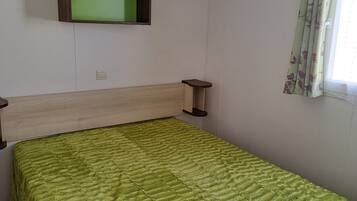 Un lit simple avec une couette verte, une tête de lit en bois, une table de chevet et un téléviseur fixé au mur.