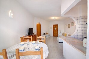 Zona pranzo con tavolo apparecchiato per quattro persone, televisione e angolo cottura con bancone e posti a sedere.