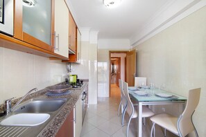 A modern kitchen with stainless steel appliances, a dining area with a glass table and chairs, and a hallway leading to another room.