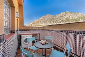 Une petite terrasse avec un lave-linge, une table et des chaises, entourée de carreaux décoratifs et offrant une vue sur la montagne.