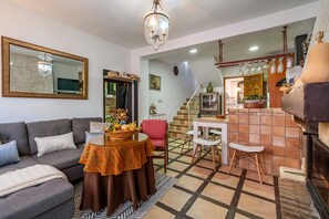 Una sala de estar con un sofá, una mesa con una cesta, una silla roja, una escalera y una zona de cocina con estufa.