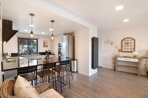 A modern kitchen with a central island, dining area with chairs, a sofa, and a TV stand.
