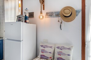 A kitchen with a white refrigerator, a hanging light bulb, a wall-mounted hat, and decorative fish pillows. - Holiday Home 'Viento De Sal' with Sea View, Shared Pool and Wi-Fi (Villa de Mazo)