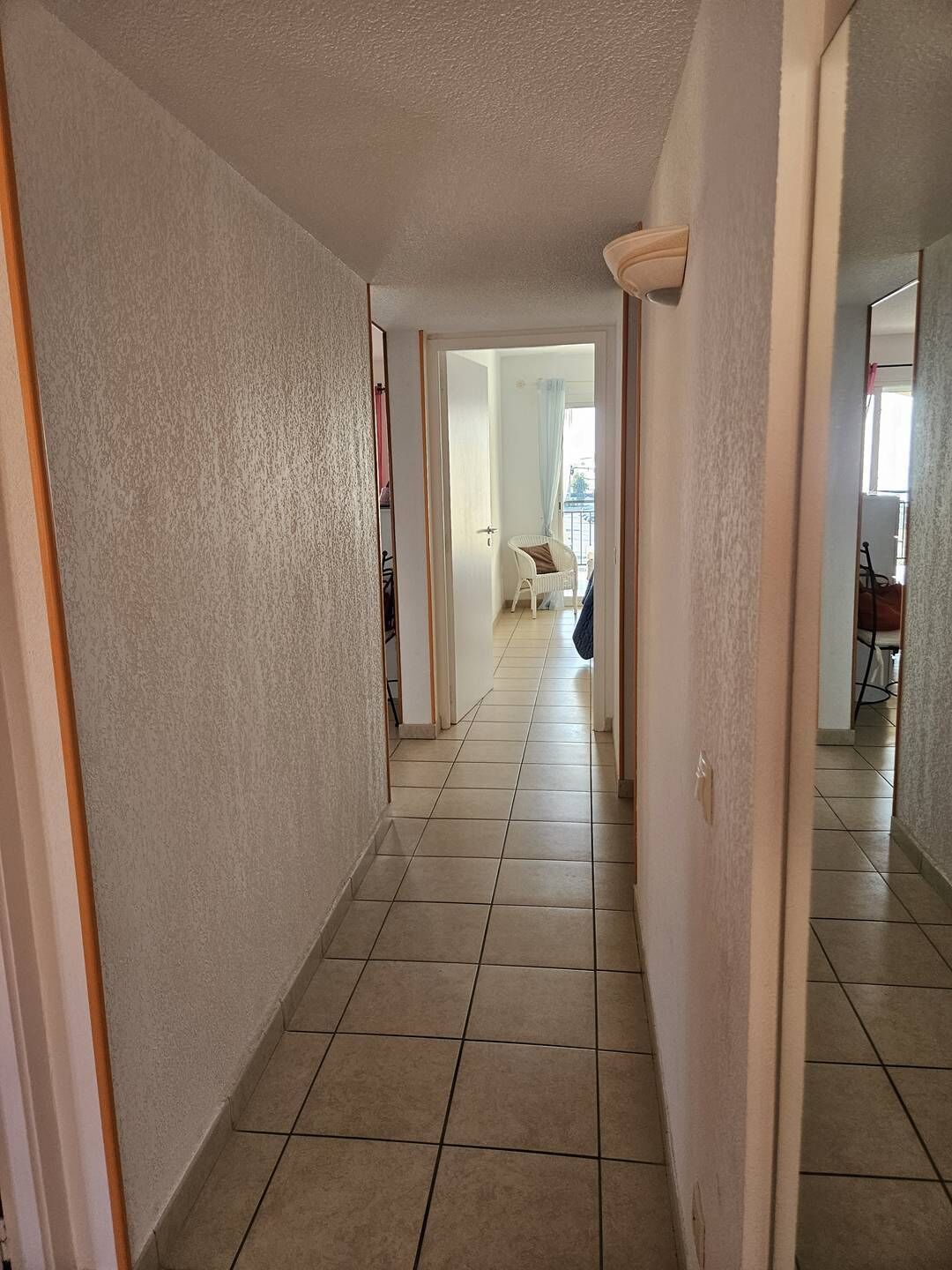 A hallway with tiled flooring leading to a balcony with a chair.