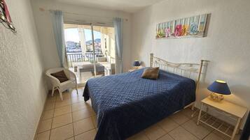 Une chambre à coucher comprenant un lit, une chaise, une table de chevet et donnant sur l’extérieur.