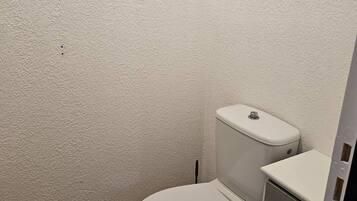 Une petite salle de bain compacte, avec des toilettes blanches, un lavabo blanc et un sol carrelé.