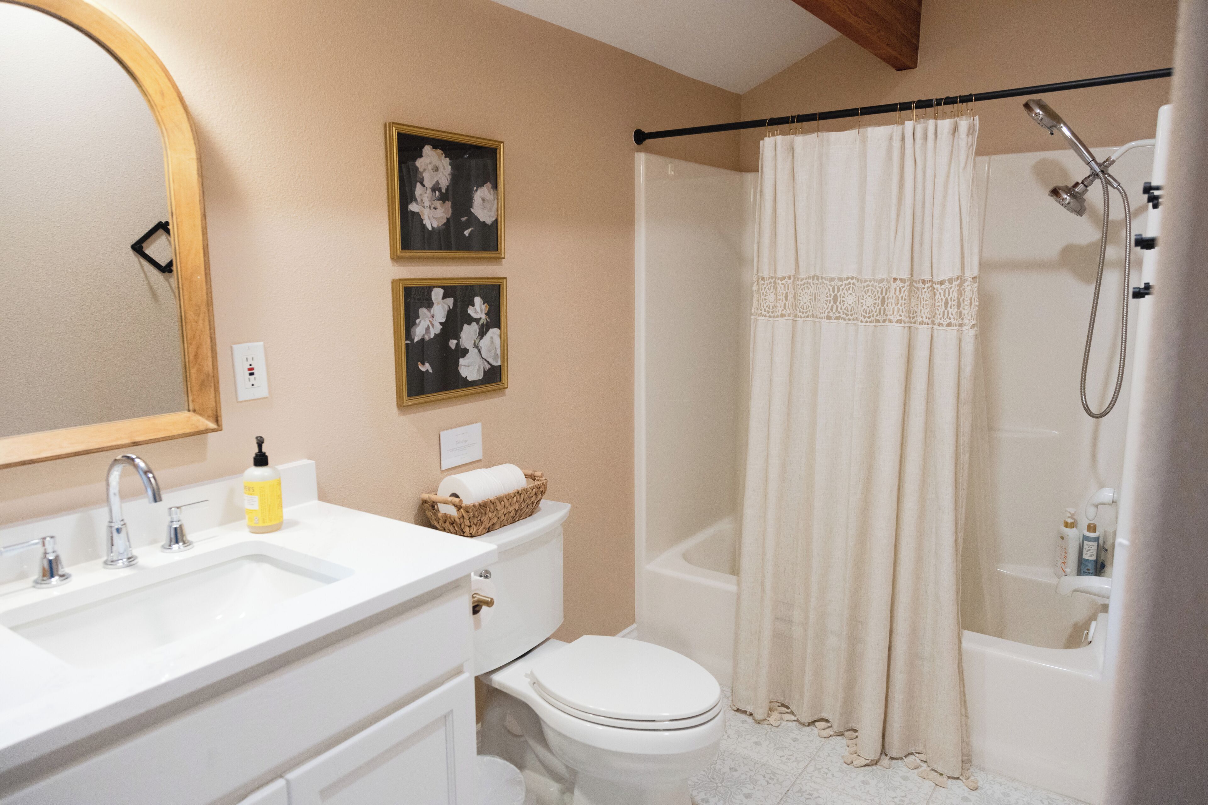 A bathroom with a white sink, toilet, and bathtub. There are two framed pictures on the wall, a shower curtain, and a towel rack.