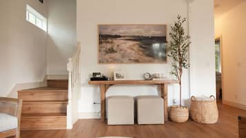 Un escalier avec des marches en bois et une rampe blanche, une console sur laquelle est posée une peinture, deux bancs rembourrés, des paniers en osier et une plante.