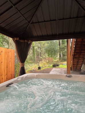 Un jacuzzi bajo una pérgola de madera con vistas a un área boscosa.