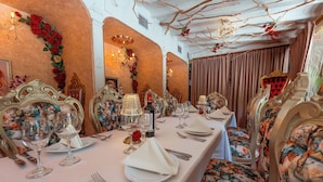 Un comedor formal con sillas ornamentadas, una mesa larga dispuesta para una comida, y detalles decorativos como flores y cortinas.