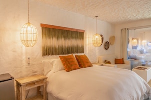 A bedroom with a large bed, a bedside table, a wooden nightstand, a wall-mounted telephone, and a window with curtains.
