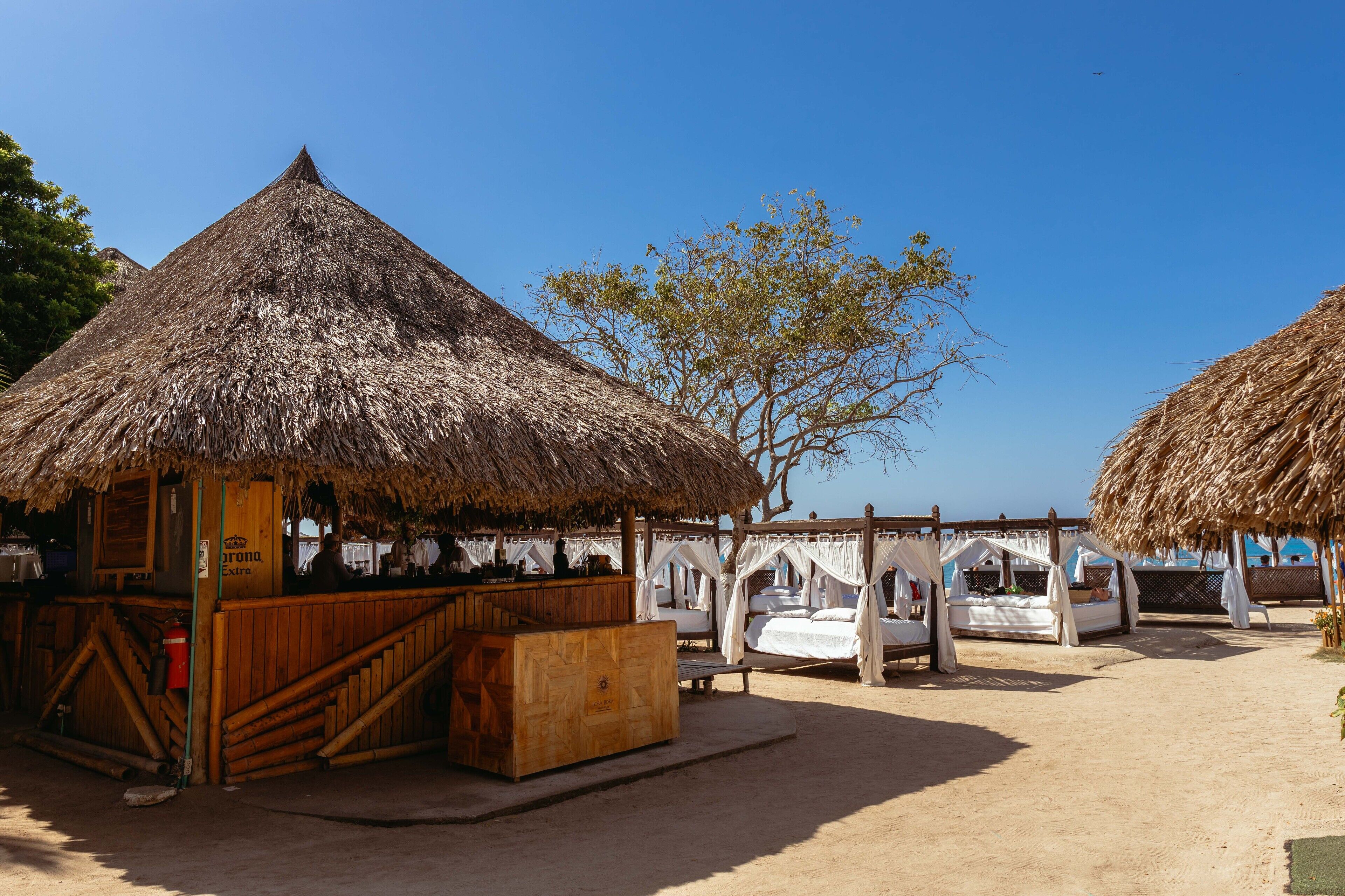 A beachside hut with a thatched roof, a wooden bar, and a canopy bed.