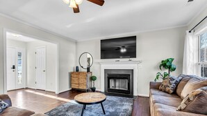 A living room with a fireplace, a television mounted above it, and a large window on the right.