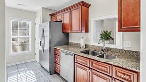 A kitchen with granite countertops, stainless steel appliances, wooden cabinets, and a window with blinds.