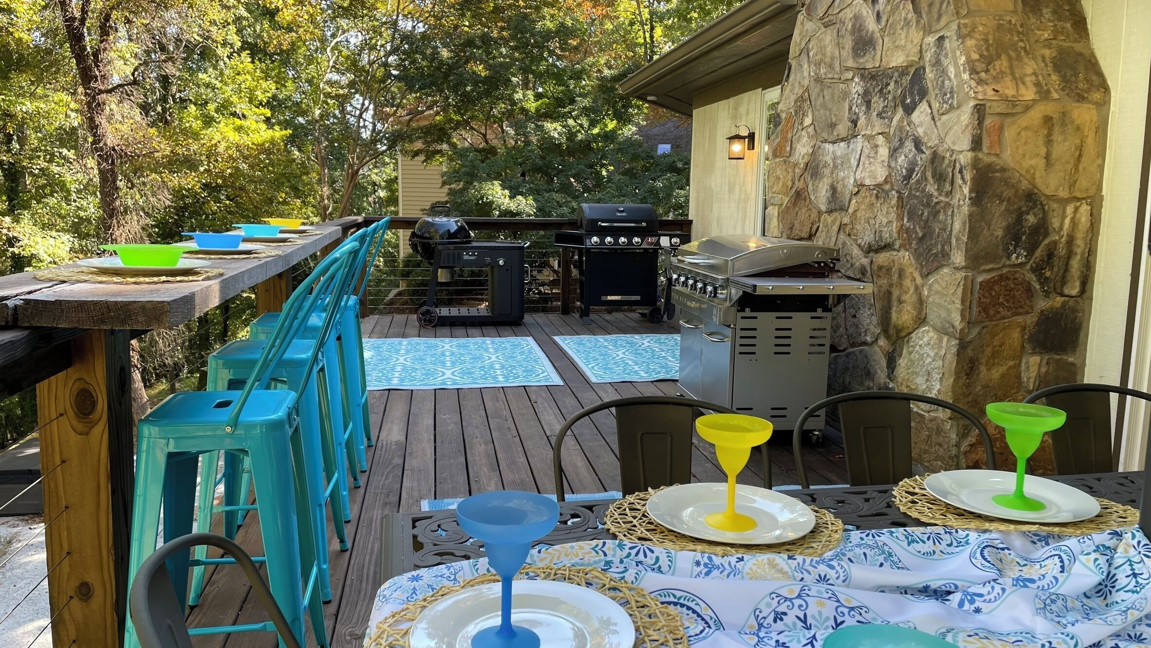 Un patio al aire libre con muro de piedra, una parrilla y una mesa lista para comer.